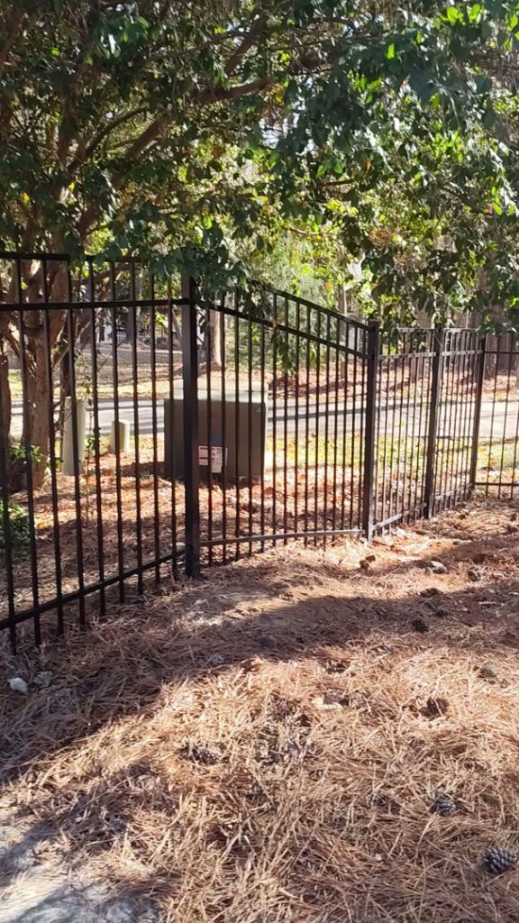 A black aluminum fence with a gate installed in a natural, wooded setting by Aguilarfence services LLC in Clayton, NC.