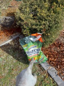A gloved hand pointing at a bag of Spectracide Triazicide Insect Killer for Lawns, showing pest control by A & A Lawn Care Service LLC in Edmond, OK.
