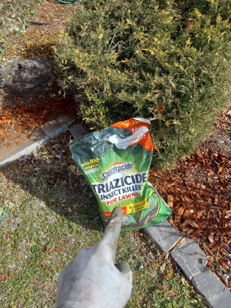 A gloved hand pointing at a bag of Spectracide Triazicide Insect Killer for Lawns, showing pest control by A & A Lawn Care Service LLC in Edmond, OK.