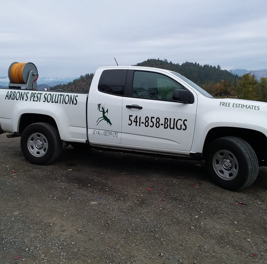 A white service truck for Arbon's Pest Solutions llc with a hose reel in the bed, ready for wildlife and pest control in Medford, OR.