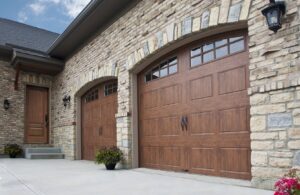 Two elegant arched brown garage doors on a stone-faced house, installed by Madison Overhead Garage Door Services in Madison, WI.