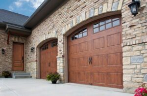 Two newly installed arched brown garage doors with windows on a stone house by Sonoran Garage Doors in Mesa, AZ