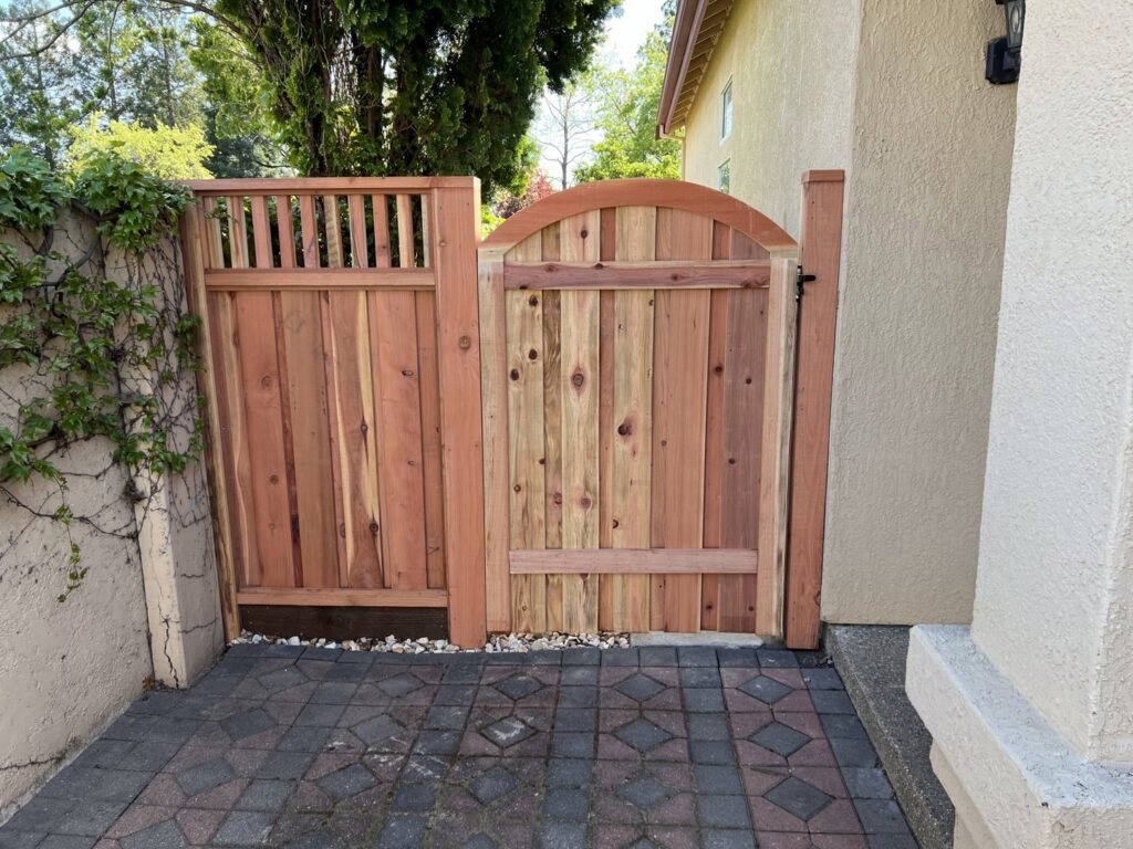 A custom arched wooden gate and side panel providing a private entry next to a home, built by Mega Fence in Thornton, CA.
