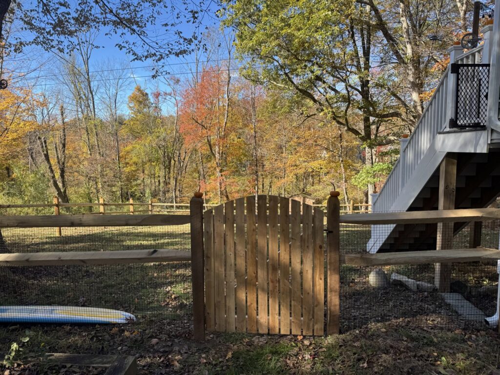 A charming arched wooden gate integrated into a split rail fence with mesh by Flanagan Fencing in Brookfield, CT.