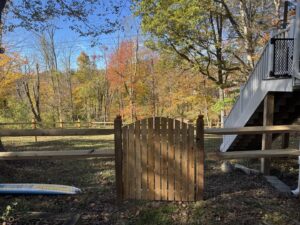 A charming arched wooden gate integrated into a split rail fence with mesh by Flanagan Fencing in Brookfield, CT.