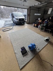 An area rug being cleaned in a garage with a cleaning van outside by Tmz Magic Carpet Cleaning in West Hartford, CT.