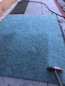 A large blue area rug being cleaned outdoors, showing a clear before and after, by JS Carpet Cleaning in San Jose, CA