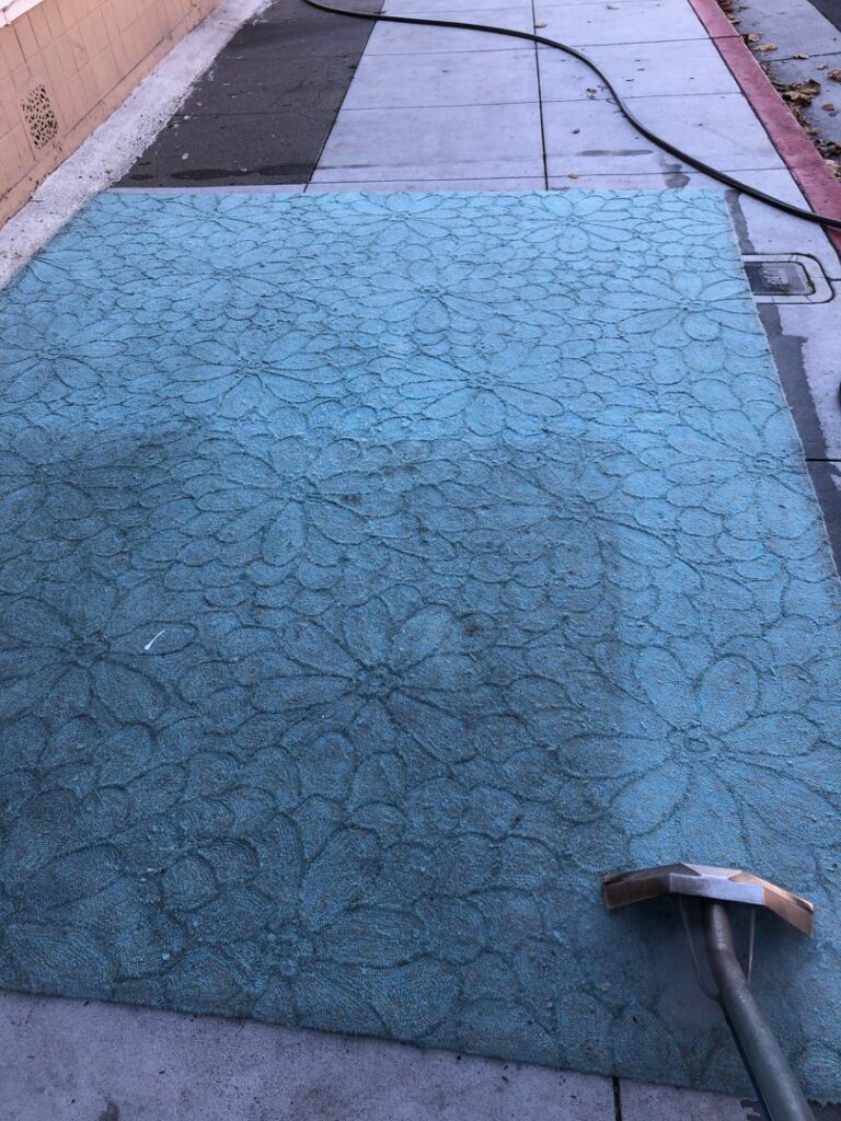 A large blue area rug being cleaned outdoors, showing a clear before and after, by JS Carpet Cleaning in San Jose, CA