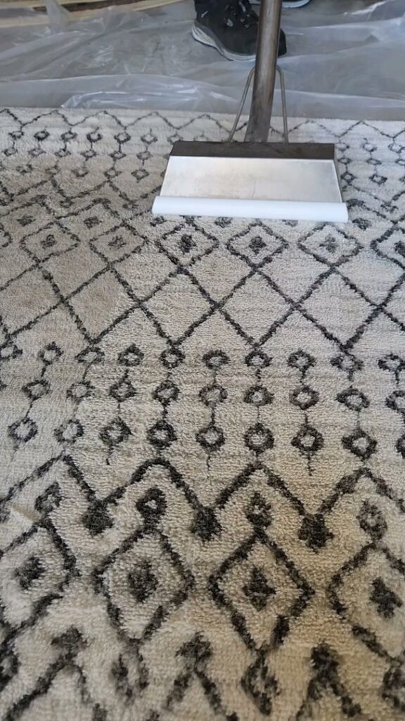 An area rug being cleaned with a steam cleaning wand, showing a clear difference, by LNC Steam Cleaning in Owasso, OK.