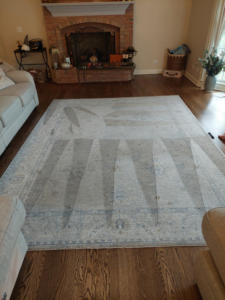 A large area rug on a hardwood floor showing distinct cleaning lines from a recent service by Proper Carpet Cleaning in Aurora, IL.