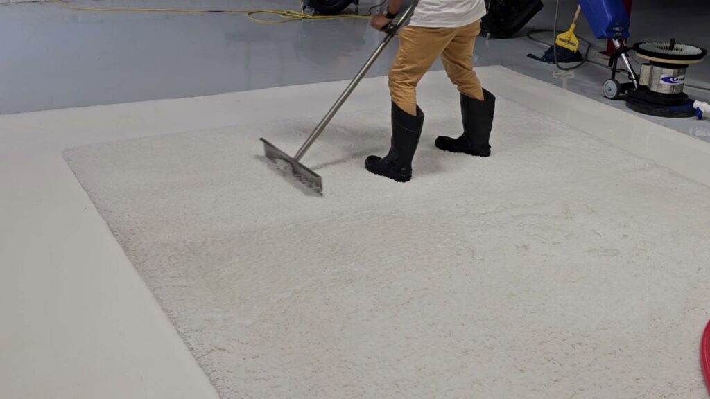 A worker using a specialized tool to clean a white area rug on a hard floor at Personal Touch Carpet Cleaning in Chicago, IL.