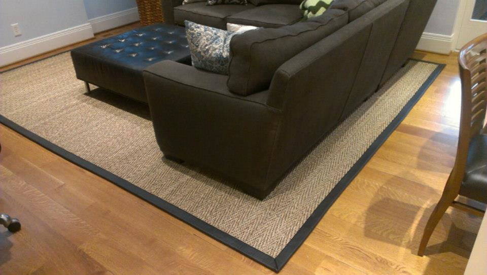 A custom area rug with a dark border placed under a sofa in a living room by Carpet Art of America in O'Fallon, MO.