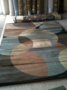 A modern area rug displayed on a carpeted floor, with carpet rolls in the background at Carpet Ends in West Springfield, MA.