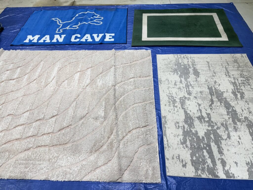 Various area rugs laid out on a blue tarp, indicating professional rug cleaning services by Strictly Tile & Carpet Care in Lansing, MI.