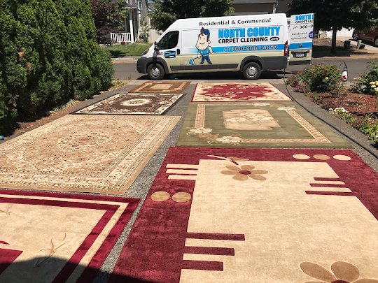 Several area rugs laid out to dry on a driveway with the North County Carpet Cleaning van in the background in Vancouver, WA