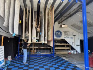 Several area rugs hanging to dry on a specialized rack after professional cleaning at C&R's Carpet Cleaning in Ellsworth, ME.