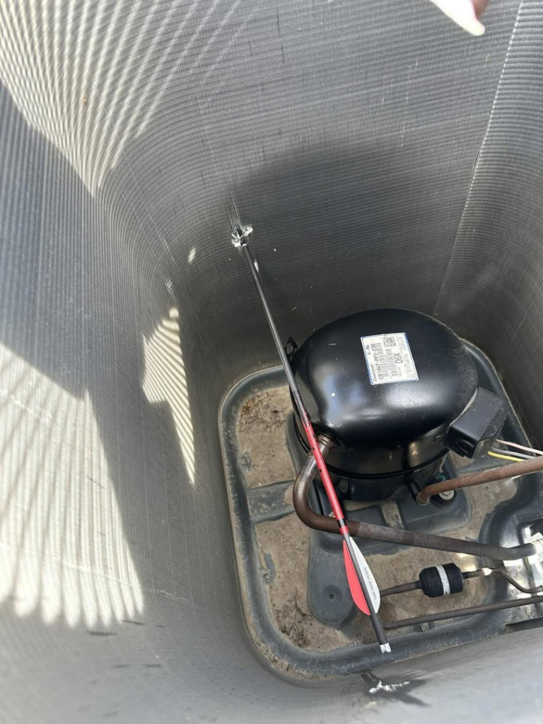 An arrow stuck inside the compressor unit of an outdoor AC system, indicating a repair job by Full Send Plumbing Heating & Cooling in Stillwater, OK.