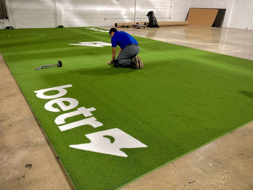A worker installing artificial turf with a custom logo in a large indoor space by Global Flooring Enterprise in Miami, FL.
