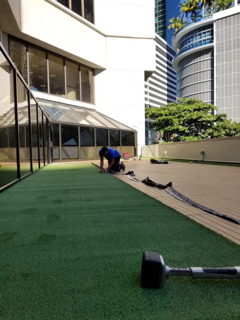 A worker installing artificial turf on an outdoor rooftop area by Global Flooring Enterprise in Miami, FL.