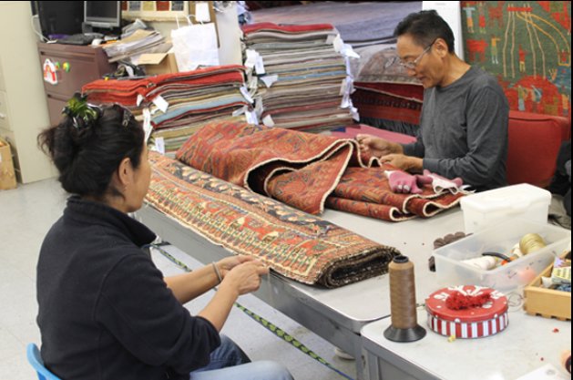 Two skilled artisans meticulously repairing a tribal rug, demonstrating services at Yayla Tribal Rugs, Inc. in Cambridge, MA.