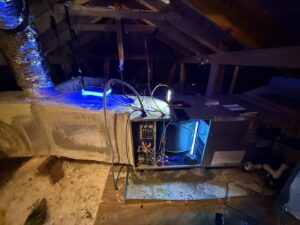 An open HVAC air handler unit with a blue UV light system installed in an attic by Gibson's Air Conditioning & Heating in Corpus Christi, TX.