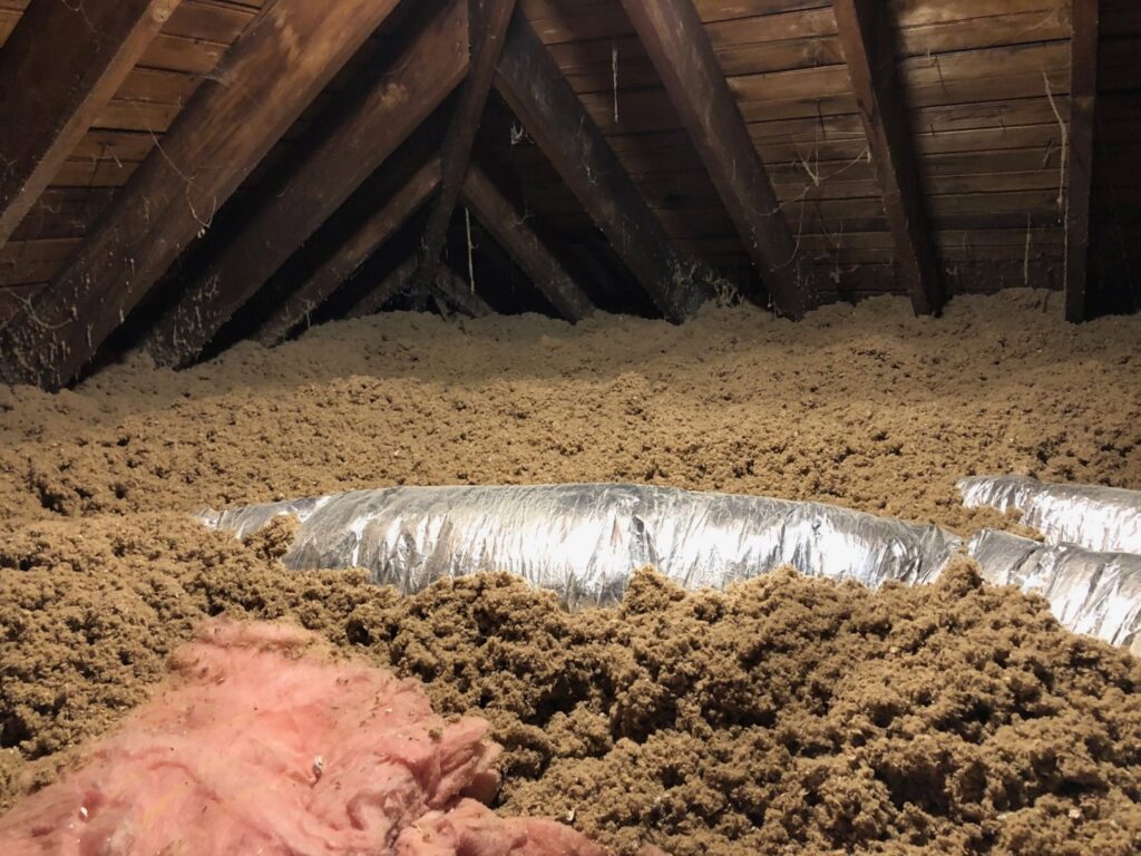 Attic with blown-in insulation and flexible HVAC ductwork installed by HomeWorks Energy in Medford, MA.