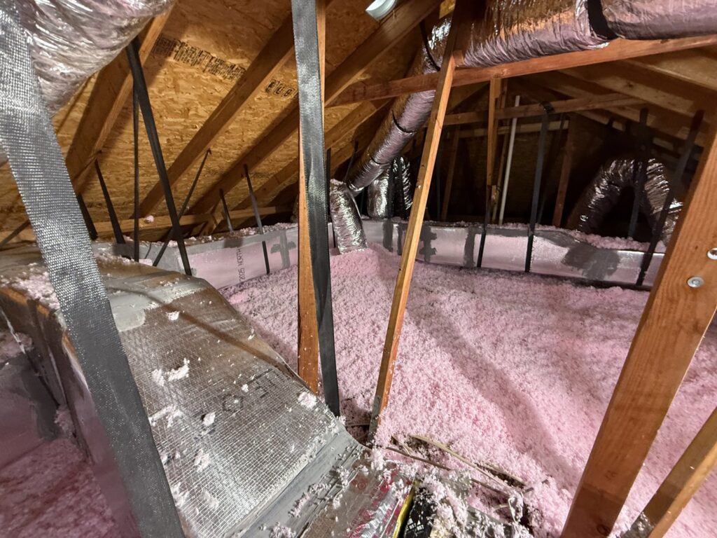Attic space showing pink blown-in insulation and flexible HVAC ductwork installed by Gibson's Air Conditioning & Heating in Corpus Christi, TX.