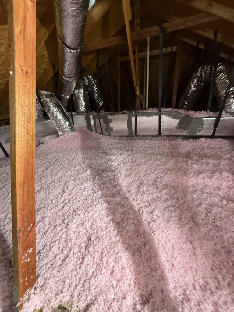 Attic space showing new pink blown-in insulation and flexible HVAC ductwork installed by Gibson's Air Conditioning & Heating in Corpus Christi, TX.