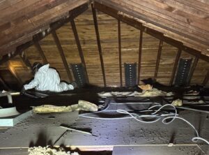 A worker in a protective suit performing attic insulation removal for Assured Energy Solutions in Frankfort, IL.