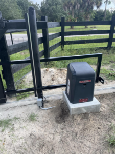 An automatic gate motor installed on a concrete pad next to a black fence by Big Bear Automatic Gates, LLC in La Belle, FL.