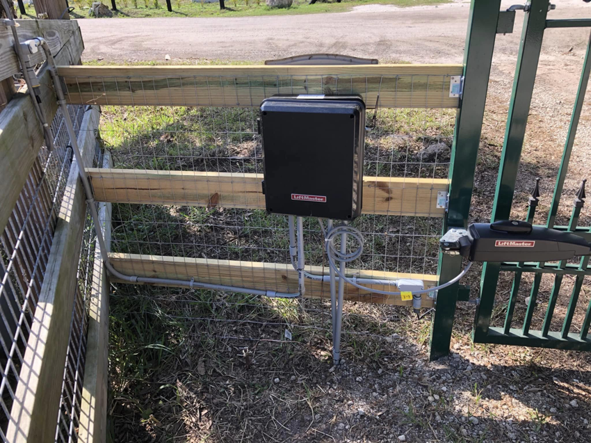 An automatic gate opener installed on a wooden and wire mesh fence by Big Bear Automatic Gates, LLC in La Belle, FL.