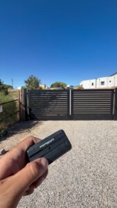 A hand holding a remote control for an automatic horizontal slat gate installed by City Iron LLC in Albuquerque, NM.