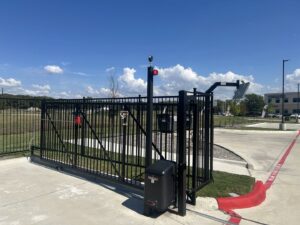 An automatic black metal sliding gate with a solar panel and security camera, installed by Iron Fence Services, LLC in Lancaster, TX.
