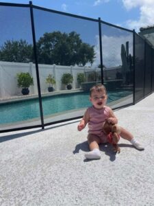 A baby safely playing next to a black mesh pool safety fence installed by All Brand Pool Fence in Fort Lauderdale, FL.
