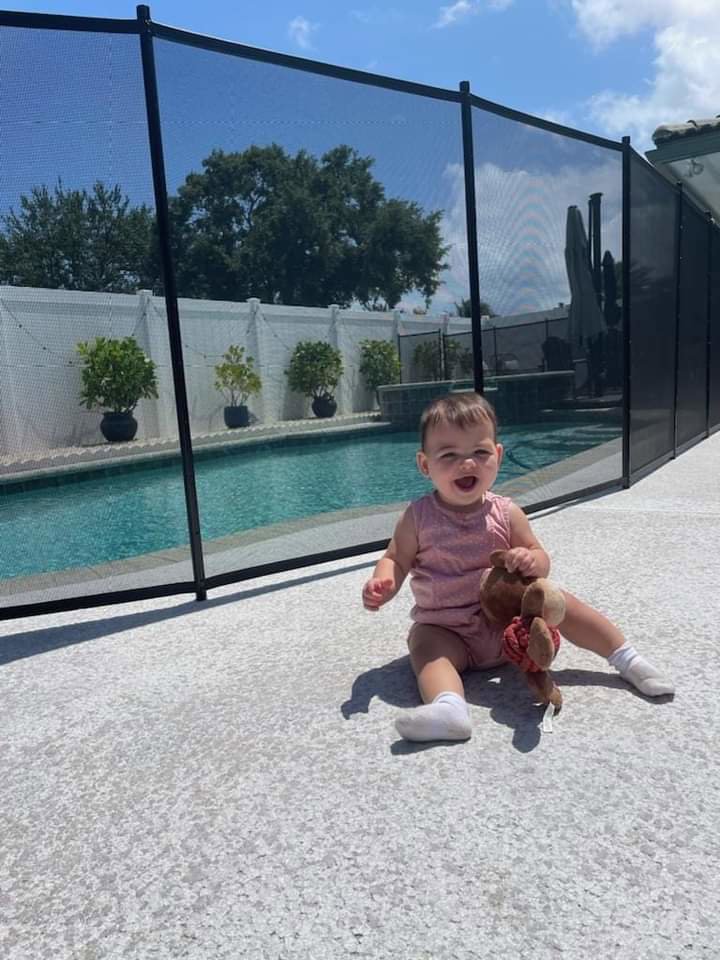 A baby safely playing next to a black mesh pool safety fence installed by All Brand Pool Fence in Fort Lauderdale, FL.