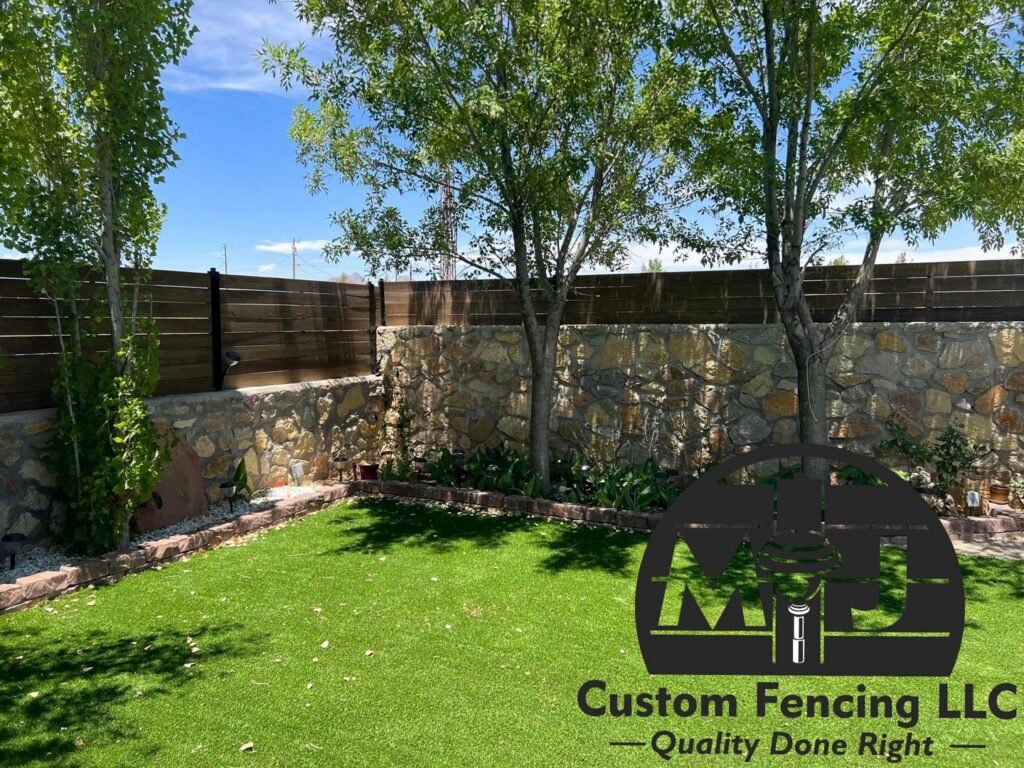 A backyard with artificial turf, trees, and a newly installed wood fence on a stone retaining wall by MJ Custom Fencing in Las Cruces, NM.