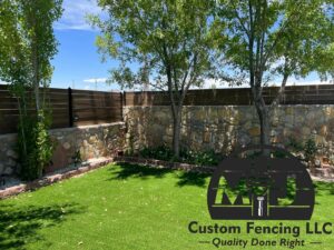 A backyard with artificial turf, trees, and a newly installed wood fence on a stone retaining wall by MJ Custom Fencing in Las Cruces, NM.