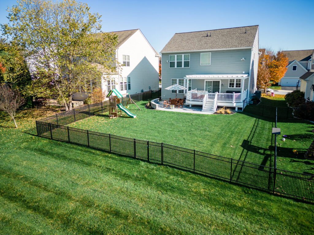 An expansive backyard featuring a black metal fence, deck, and playset installed by Integrous in Gap, PA