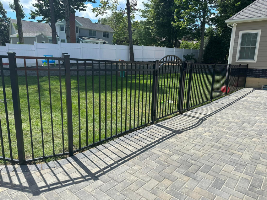 A backyard featuring a new black metal fence with an arched gate installed by Fenced Up, LLC in Ravena, NY.
