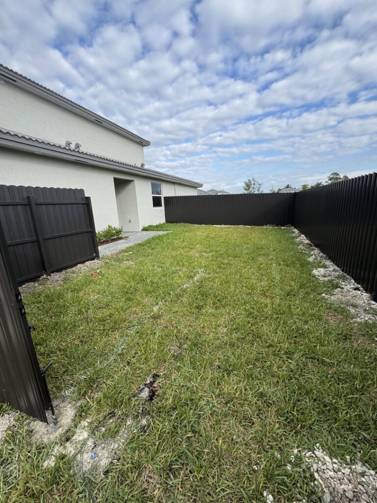 A backyard enclosed by a dark gray scalloped fence with a matching gate by Osuna Ornamental Fences & Gates in Cutler Bay, FL.