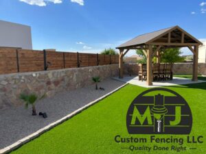 A backyard featuring a custom wood fence on a stone wall, artificial turf, and a gazebo installed by MJ Custom Fencing in Las Cruces, NM.
