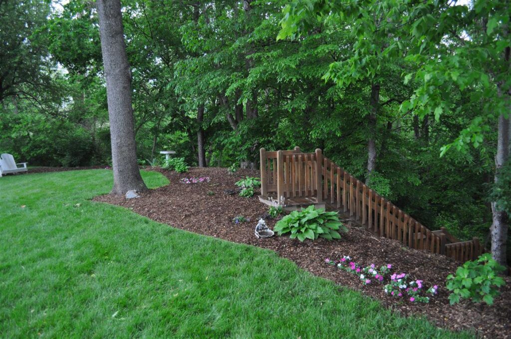 A beautifully landscaped backyard featuring a wooden staircase and mulched garden beds by Kustom Lawn Kare LLC in Greenwood, IN.