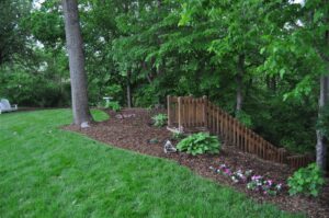 A beautifully landscaped backyard featuring a wooden staircase and mulched garden beds by Kustom Lawn Kare LLC in Greenwood, IN.