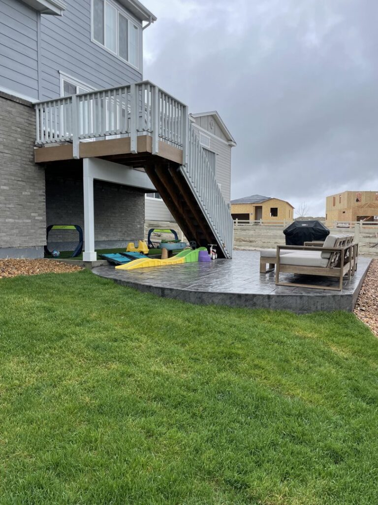 A well-maintained backyard lawn adjacent to a modern patio and outdoor seating by The Fisherman Landscaping LLC in Westminster, CO.