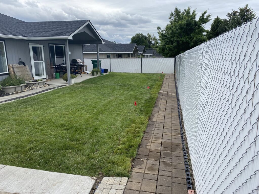 A well-maintained backyard lawn with a paved pathway, showing professional care by McLain Lawn & Landscape in Spokane, WA.