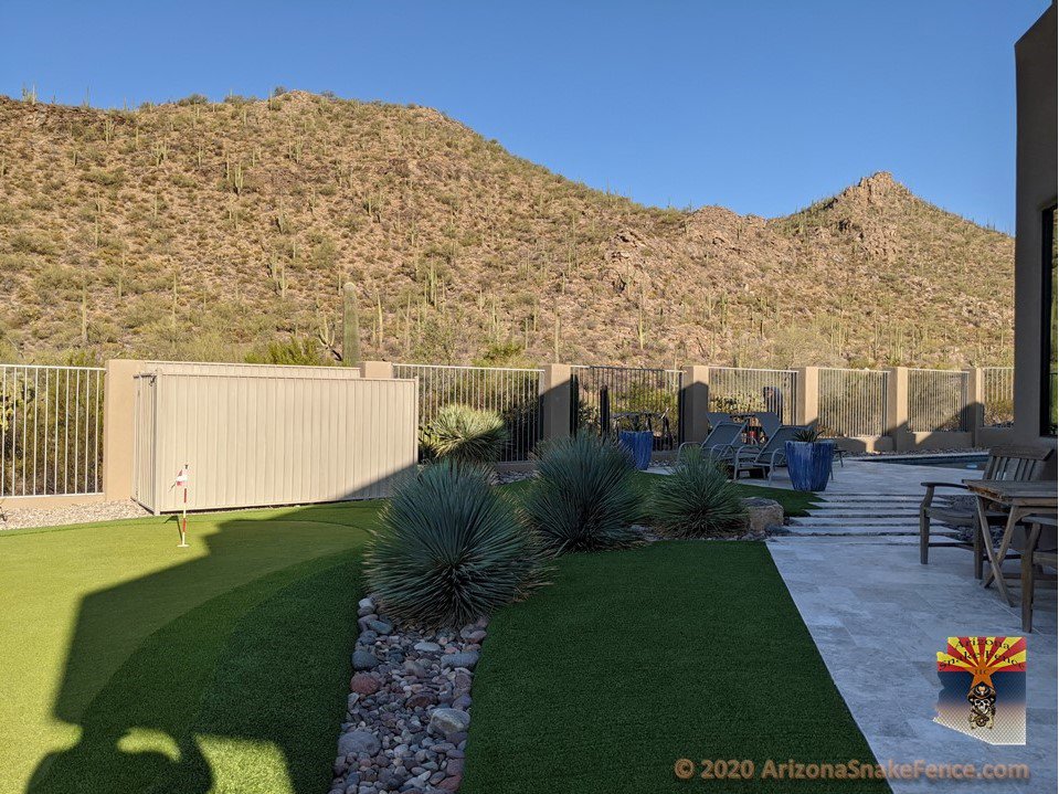 A light-colored metal snake fence with a block base protecting a backyard with artificial turf, installed by Arizona Snake Fence LLC in Tucson, AZ