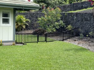 A backyard featuring a new black metal fence with a gate and a rockwall by Fence, Gates and Rockwalls in Kailua-Kona, HI