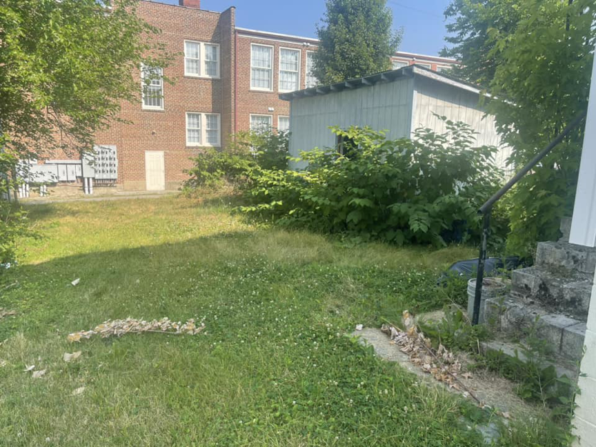 A backyard with partially mowed grass and untrimmed bushes near a shed, during a landscaping job by Elliott's Lawn Care & Landscaping in Lexington, KY.