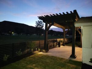 A backyard patio with a pergola and black horizontal slat fence illuminated at dusk by Allied Fence Co in Tulsa, OK.