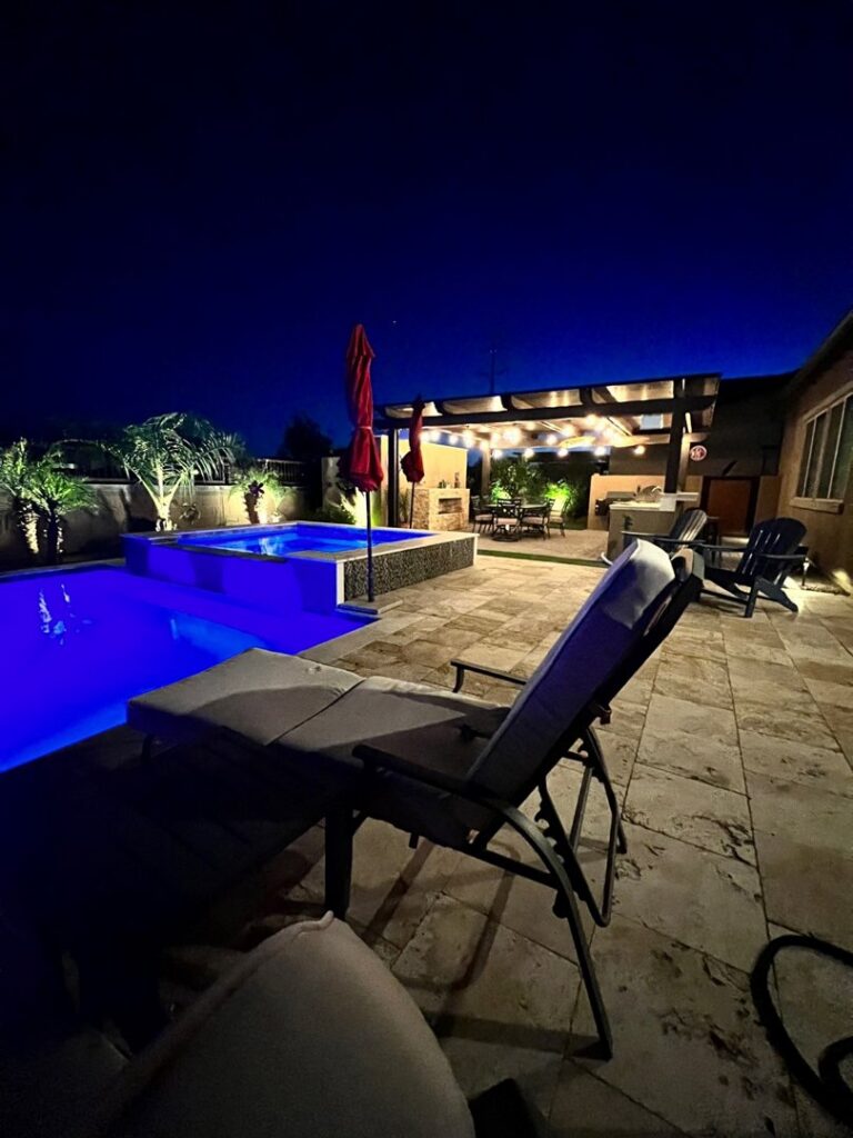 A backyard swimming pool illuminated with blue lighting at night by Blue Magic Pools and More Inc. in Gilbert, AZ.